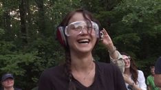 a woman wearing goggles and talking on her cell phone while standing in the woods