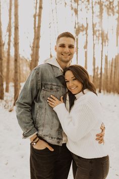 a man and woman standing next to each other in the snow with trees behind them