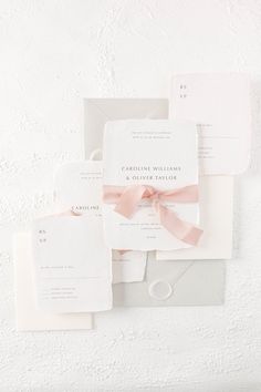 the wedding stationery is laid out on top of each other, with pink ribbon