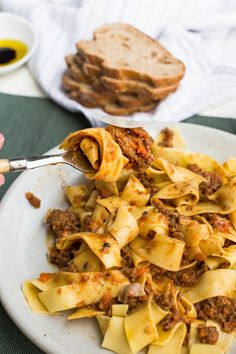 a white plate topped with pasta covered in meat and sauce next to slices of bread