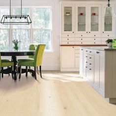 a dining room table with green chairs next to a window and white cabinets in the background