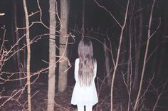 a woman standing in the middle of a forest at night with her back to the camera