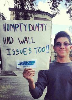 a man holding up a sign that says humpty dumppy had wall issues too