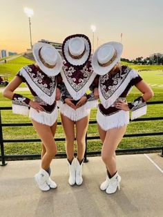 three women in matching outfits posing for a photo at a football game with the sun setting behind them