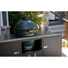 a big green egg sitting on top of a metal cabinet in front of a house