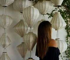 a woman is standing in front of many white lanterns hanging from the wall and looking at them