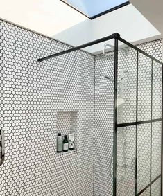 a white tiled bathroom with black and white tile on the walls, shower head, and toilet paper holder