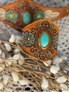 two brown and turquoise leather cufflinks with flowers on them sitting next to some white beads