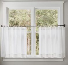 a window with white curtains in front of it and trees outside the window sill