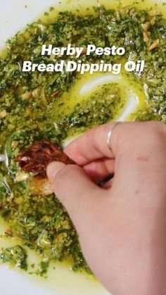 a person is dipping pesto onto bread dipping oil in a white bowl with the words, herb pesto bread dipping oil