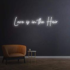 a neon sign that says love is in the hair next to a chair and table