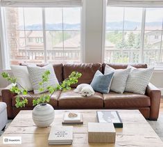 a brown leather couch sitting in front of a window next to a wooden coffee table