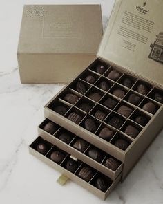 an open box of chocolates sitting on top of a marble counter next to a gold package