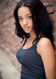 a beautiful young woman leaning against a brick wall