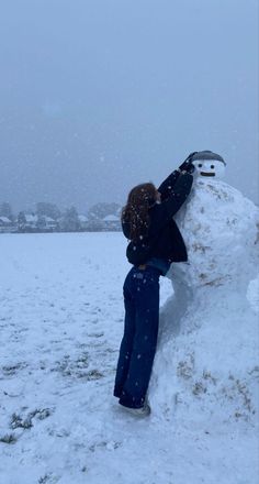 a person building a snowman in the middle of a field with their hands on it