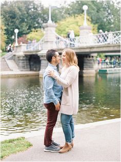 a man and woman standing next to each other in front of a pond with bridge