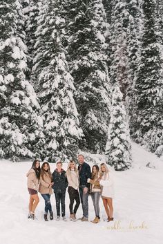 a group of people standing next to each other in front of snow covered evergreen trees