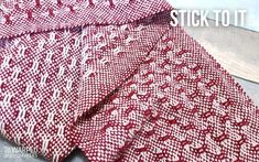 a red and white knitted blanket sitting on top of a wooden floor with the words stick to it