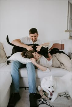 a man and woman are sitting on a couch with their two dogs, one black and the other white