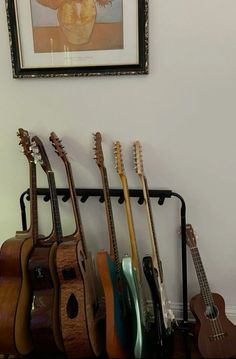 there is a guitar rack in the corner with several guitars on it and a framed picture above