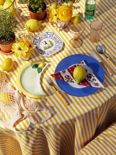 a table topped with plates covered in food next to lemons and flowers on top of a yellow striped table cloth