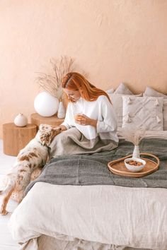 a woman sitting on a bed with her dog and looking at the phone in front of her