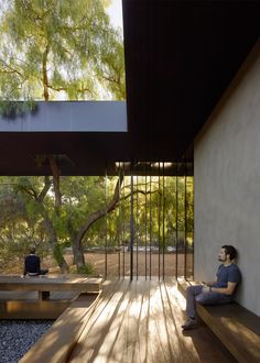 a person sitting on a wooden bench in front of a building with trees and water