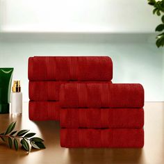 four red towels stacked on top of each other next to a green plant and perfume bottle