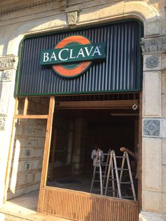 two men working on the outside of a building with a sign that reads baclava