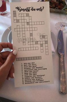 a person is holding up a crossword puzzle piece in front of a table with silverware and utensils