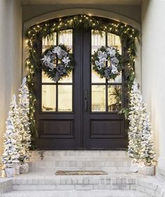 two christmas wreaths on the front door of a house with lights and garland around them