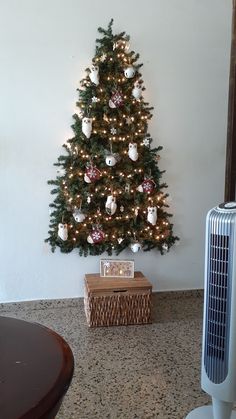 a christmas tree with ornaments on it and a fan in the corner next to it