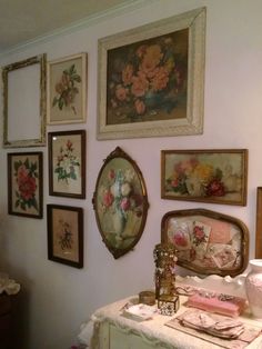 there are many framed pictures on the wall next to a table with a vase and other items