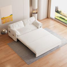 a white couch sitting on top of a hard wood floor next to a large window