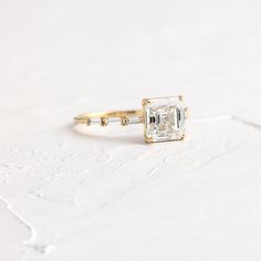 an engagement ring with a square cut diamond and two small diamonds on each side, sitting on a white surface