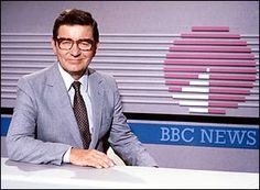 a man in a suit and tie sitting at a desk with a news logo behind him