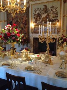 a dining room table is set with gold dishes and candles