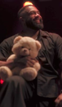 a man is holding a teddy bear in his lap while sitting on a chair at a concert