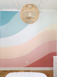 a room with a bed and a wall painted in shades of pink, blue, orange and white