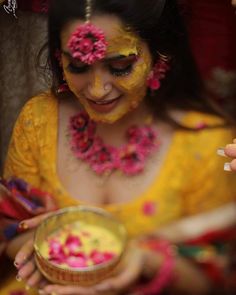 a woman in yellow is holding a bowl with flowers on it and her face painted