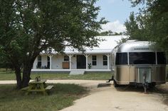 an rv parked in front of a white house next to a picnic table and trees