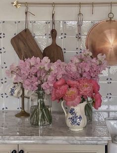 pink flowers are in vases on the kitchen counter next to pots and pans