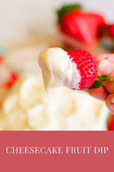 a hand holding a piece of cheesecake fruit dip with strawberries in the background