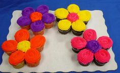 cupcakes decorated with colorful icing and flowers on a white cloth, ready to be eaten