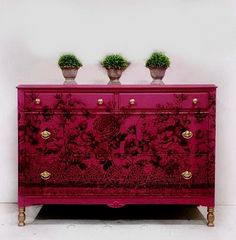 a pink dresser with two potted plants on top and an angel decoration above it