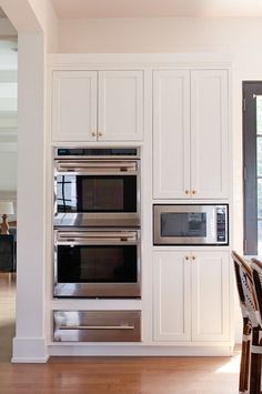 a kitchen with white cabinets and stainless steel ovens in the wall, along with a dining room table