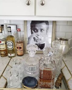 an assortment of liquor bottles and glasses sitting on a kitchen counter with a framed photograph in the background