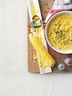 a bowl of corn on the cob next to two spoons and a napkin