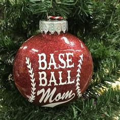 a red ornament hanging from a christmas tree with base ball mom written on it