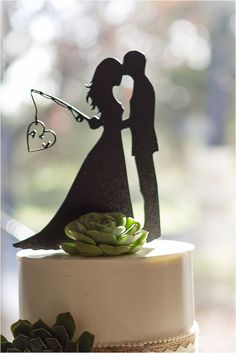 a wedding cake with a silhouette of a bride and groom holding a heart on top